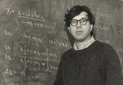 black and white photo of Richard Lewontin standing in front of a chalkboard covered in equations